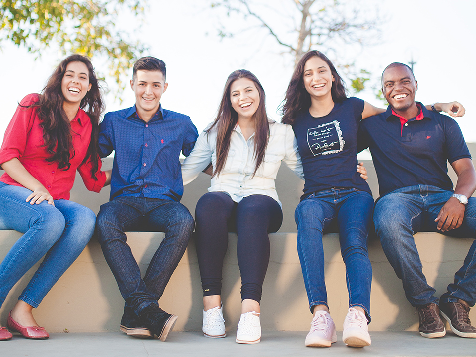five young adults sitting on a bench 