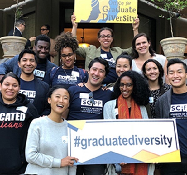 a group of graduate students stand smiling with a sign that says #graduatediversity